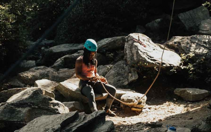 a person wearing rock climbing gear rests on a rock on an outward bound trip for lgbtq teens